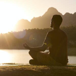 Man Meditating Doing Yoga By Lake And Mountains At Sunset