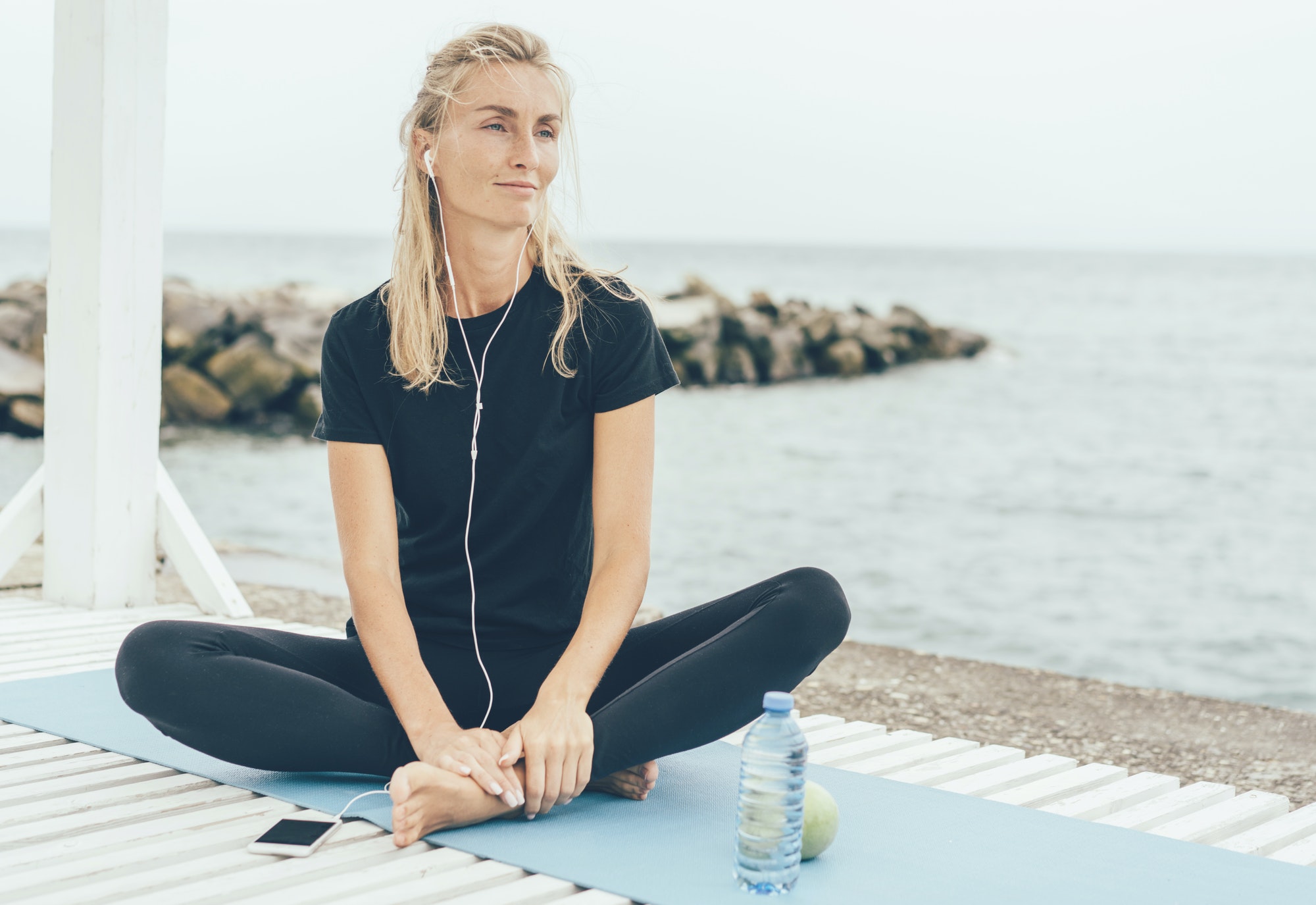Woman resting outside after sports workout and listening to music or meditation on headphones.
